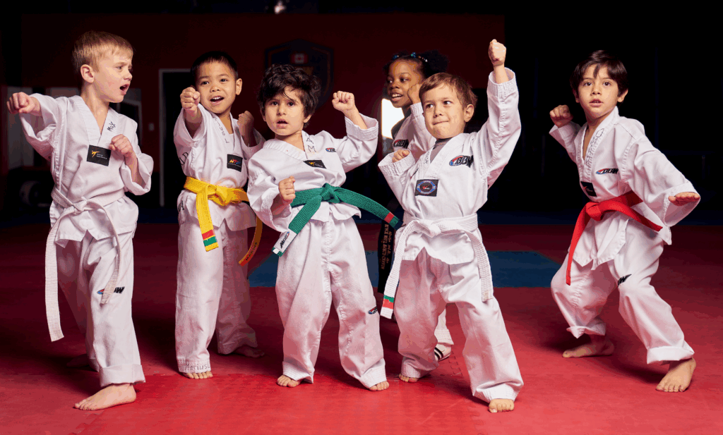 A diverse group of junior martial arts students in white uniforms performing a powerful kihap shout during their martial arts for kids session to build self confidence.