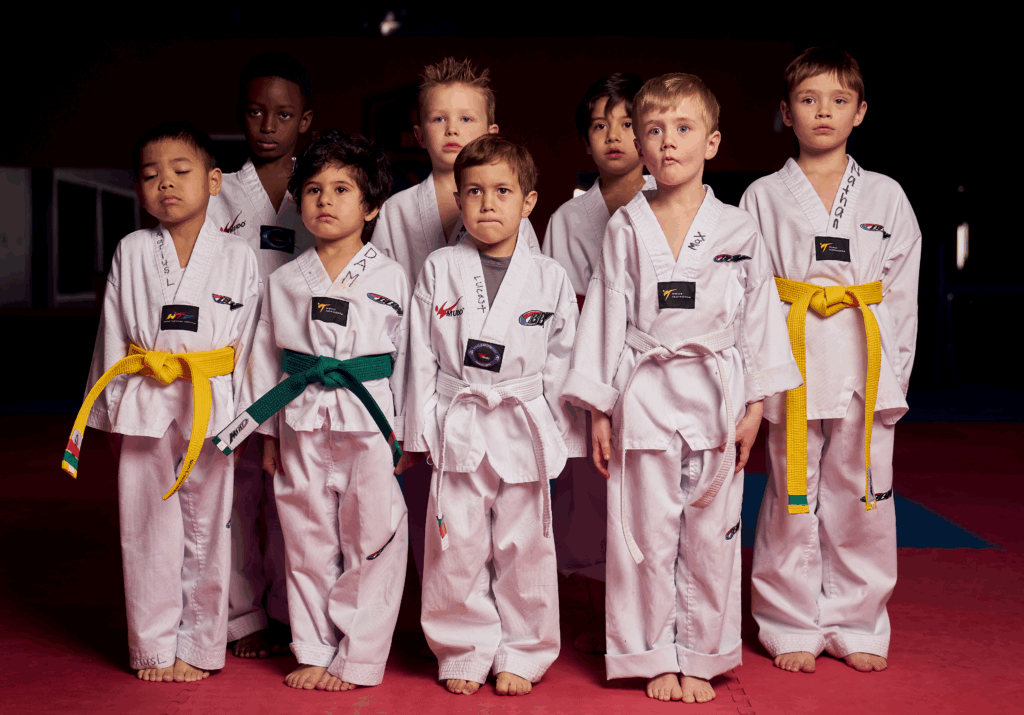 A group of young students in white uniforms and colored belts participating in a children's martial arts program at our youth fitness facility.