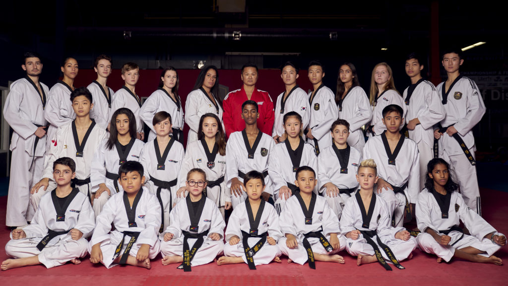 A diverse group of children and adults posing together after a successful taekwondo training session at our Toronto fitness center.